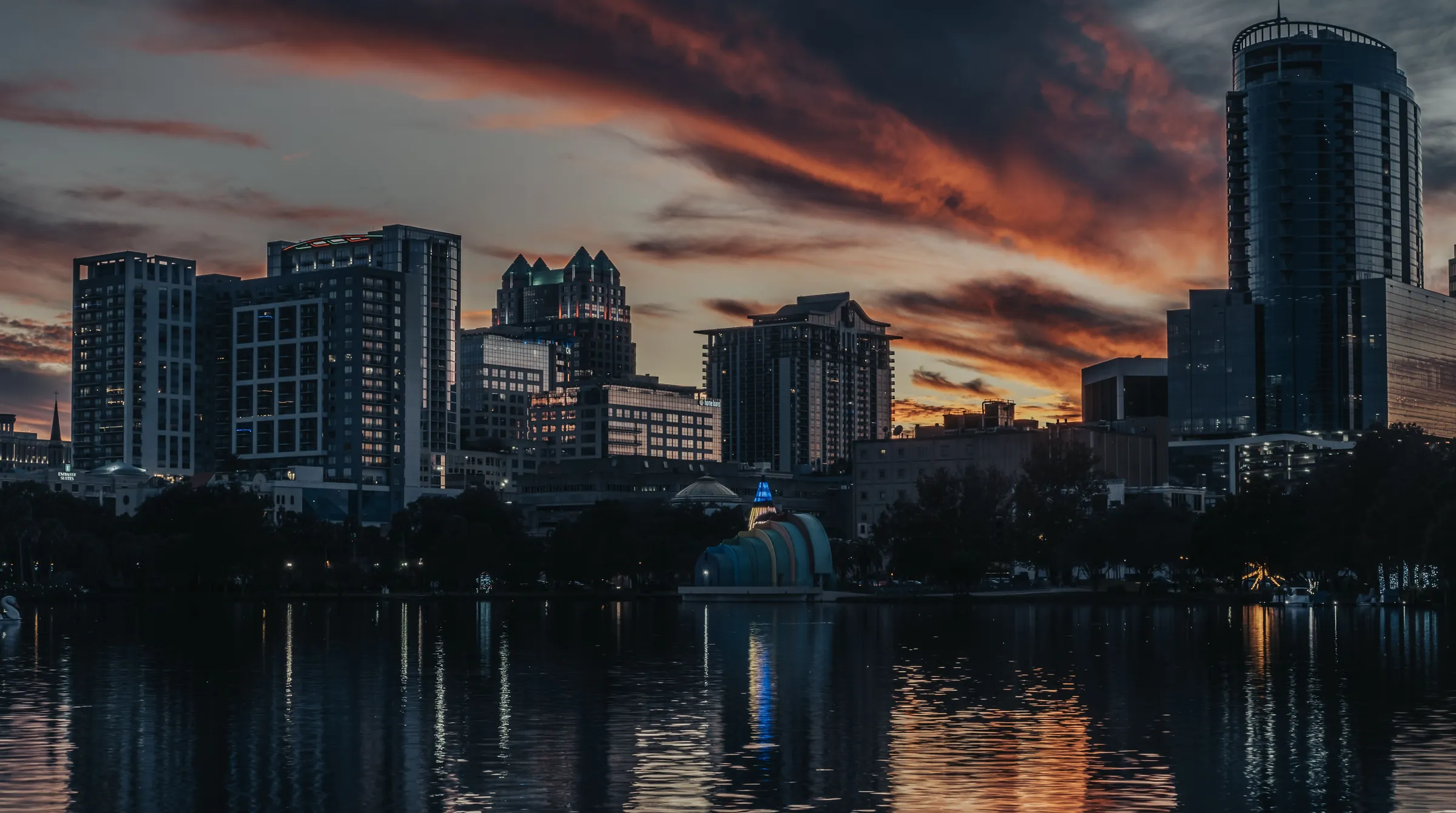 The downtown Orlando skyline at dusk, office towers reflected in a lake under an orange-streaked sky