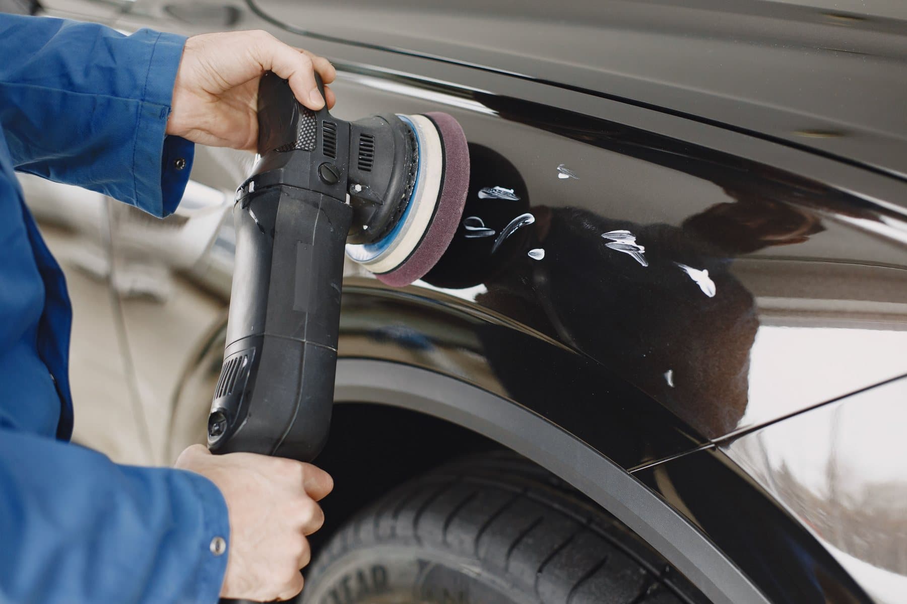 Hands holding a dual-action polisher against the wing of a black car