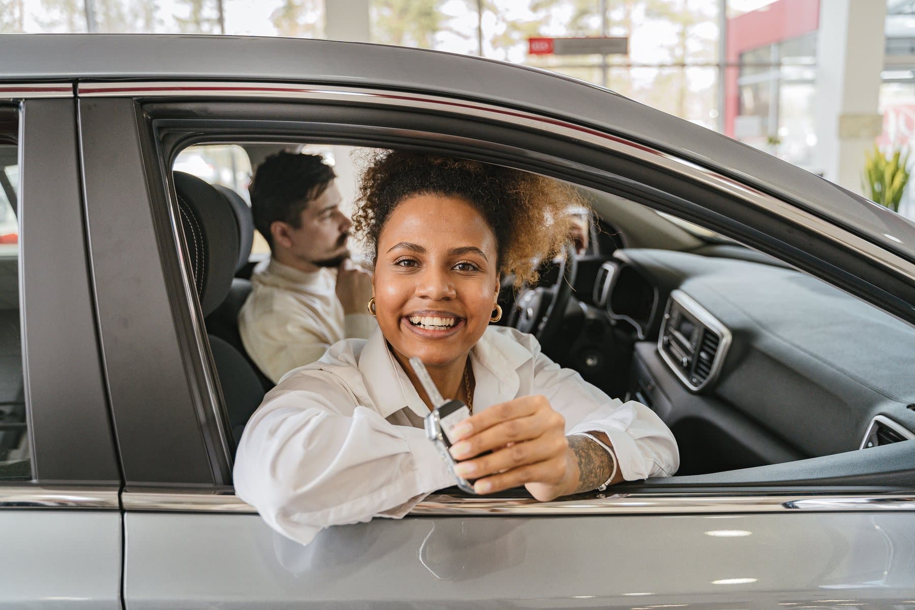 A smiling driver leaning out of a clean silver car window holding up the key. A photo from Verity Detail Studio, the sample auto detailing website.