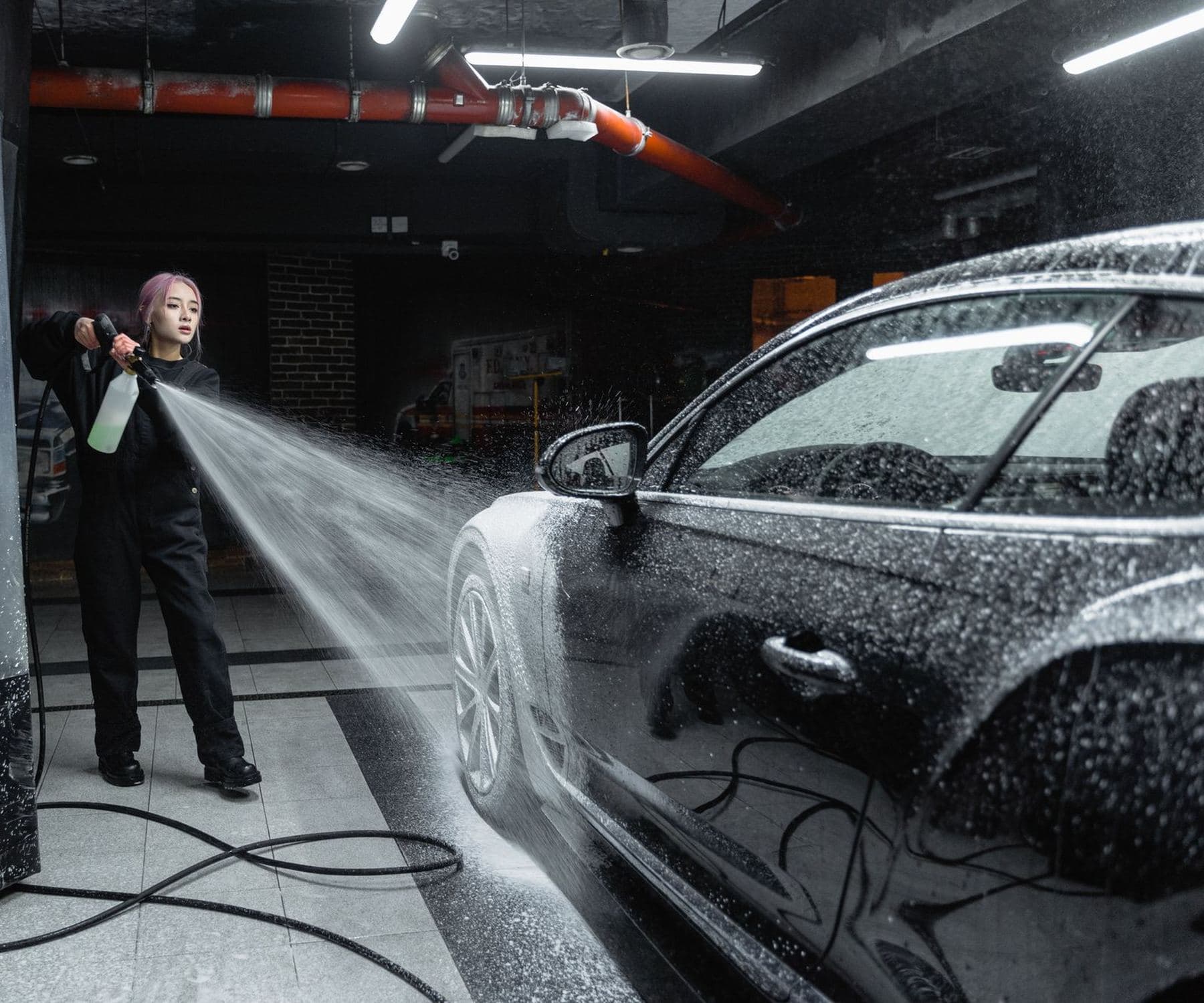 A woman spraying foam over a car in a wash bay