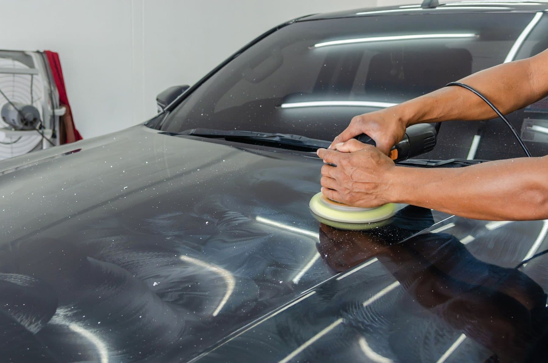 A polisher with a yellow foam pad on a black hood, fine swirl marks showing in the unpolished paint around it