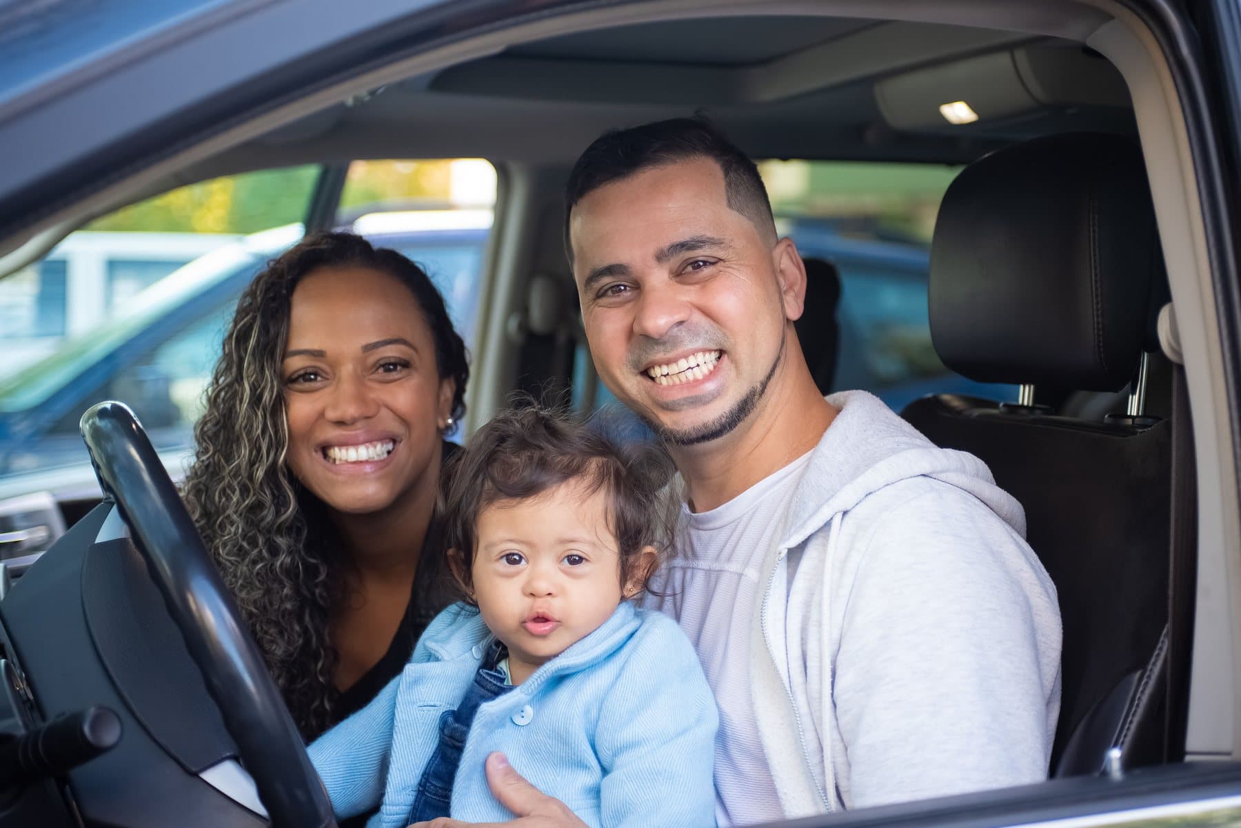 A smiling family of three sitting together in the front of their car. A photo from Cypress Line Auto Repair, the sample auto repair website.