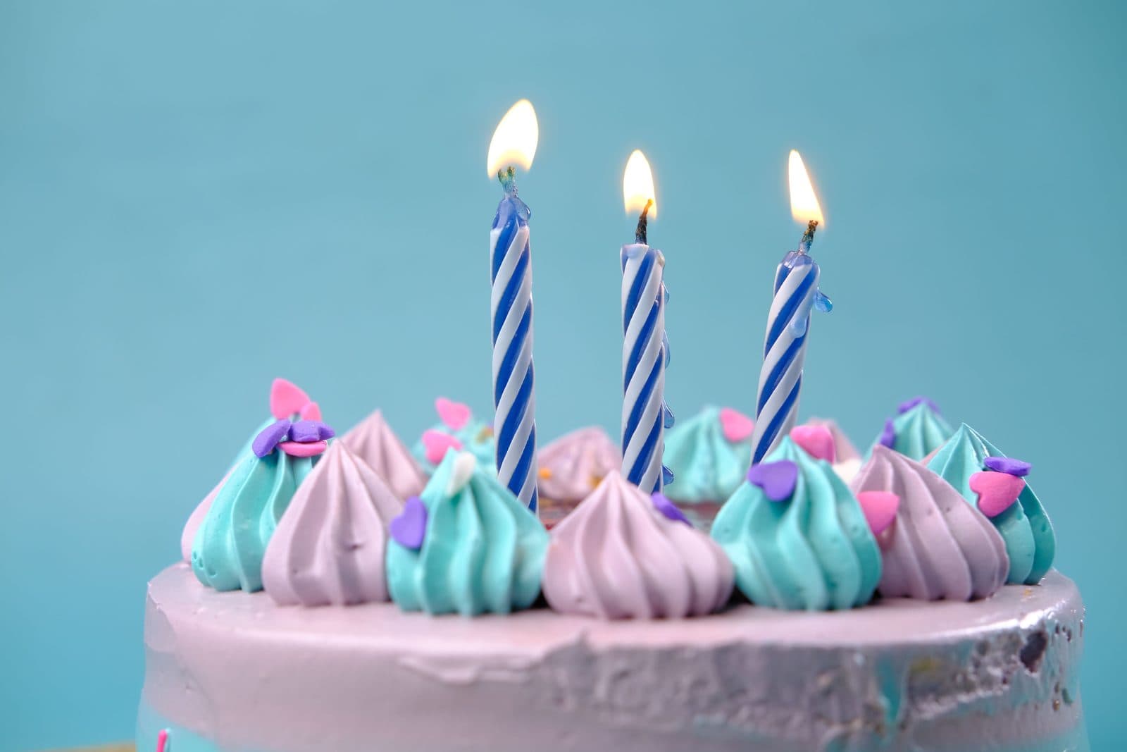 Pastel birthday cake with teal and lilac frosting swirls and three lit candles. A photo from Sugar & Crumb Bakery, the sample bakery website.