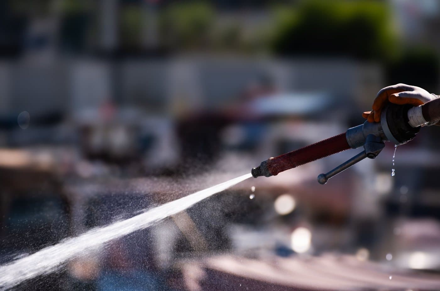 A gloved hand holding a high-pressure water nozzle, a hard jet of water leaving it