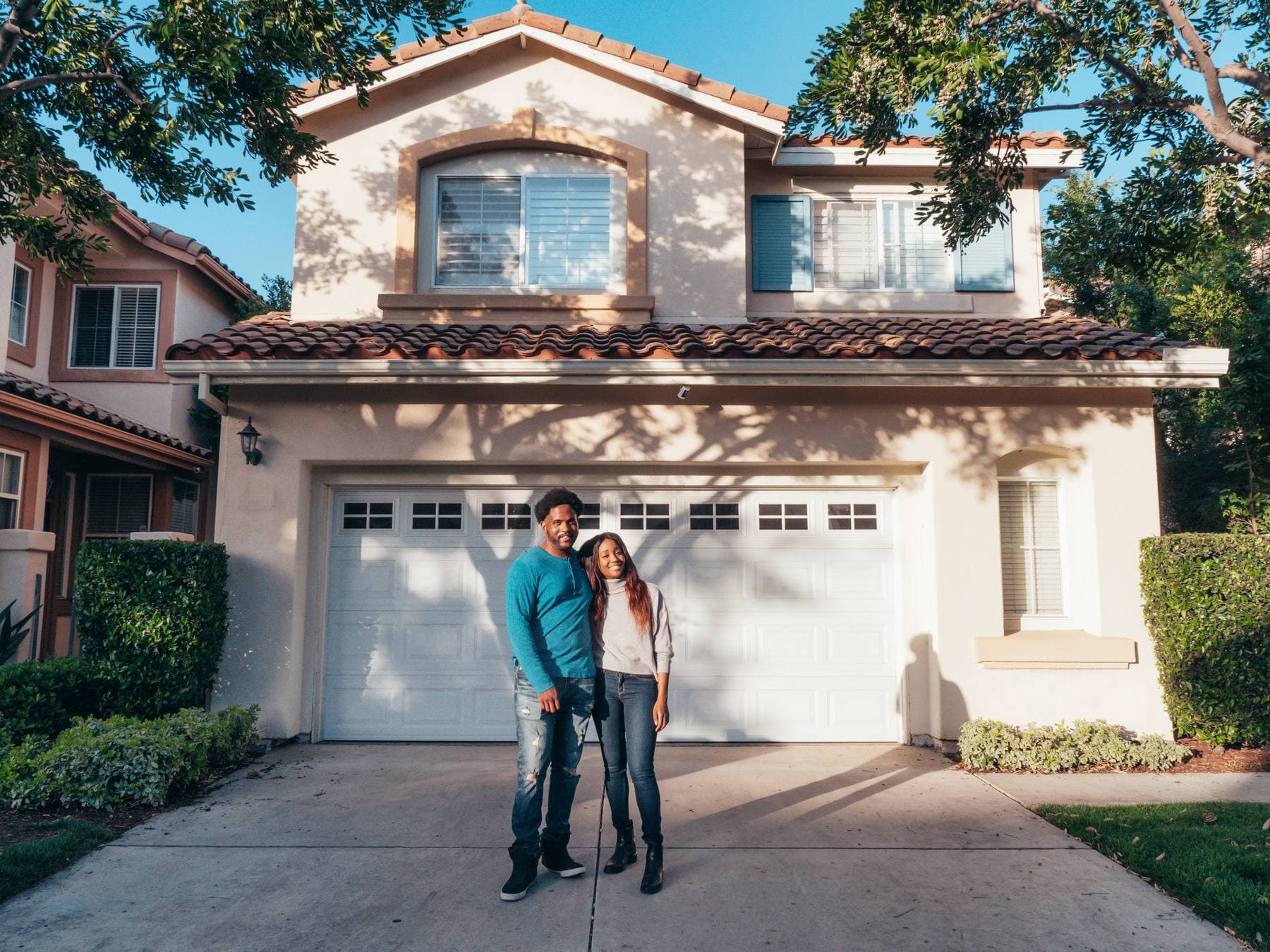 A couple standing on the driveway in front of their closed garage door. A photo from Ironleaf Garage Doors, the sample garage door repair website.