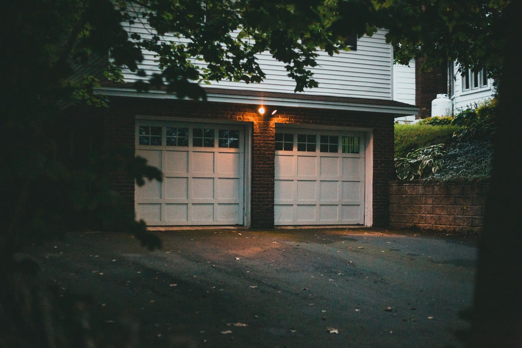 Two carriage-style garage doors lit by a porch light at dusk