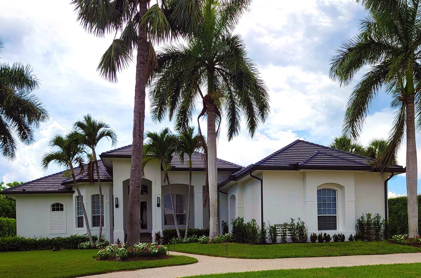 A white single-story Florida stucco home with a low hip roof under tall palms