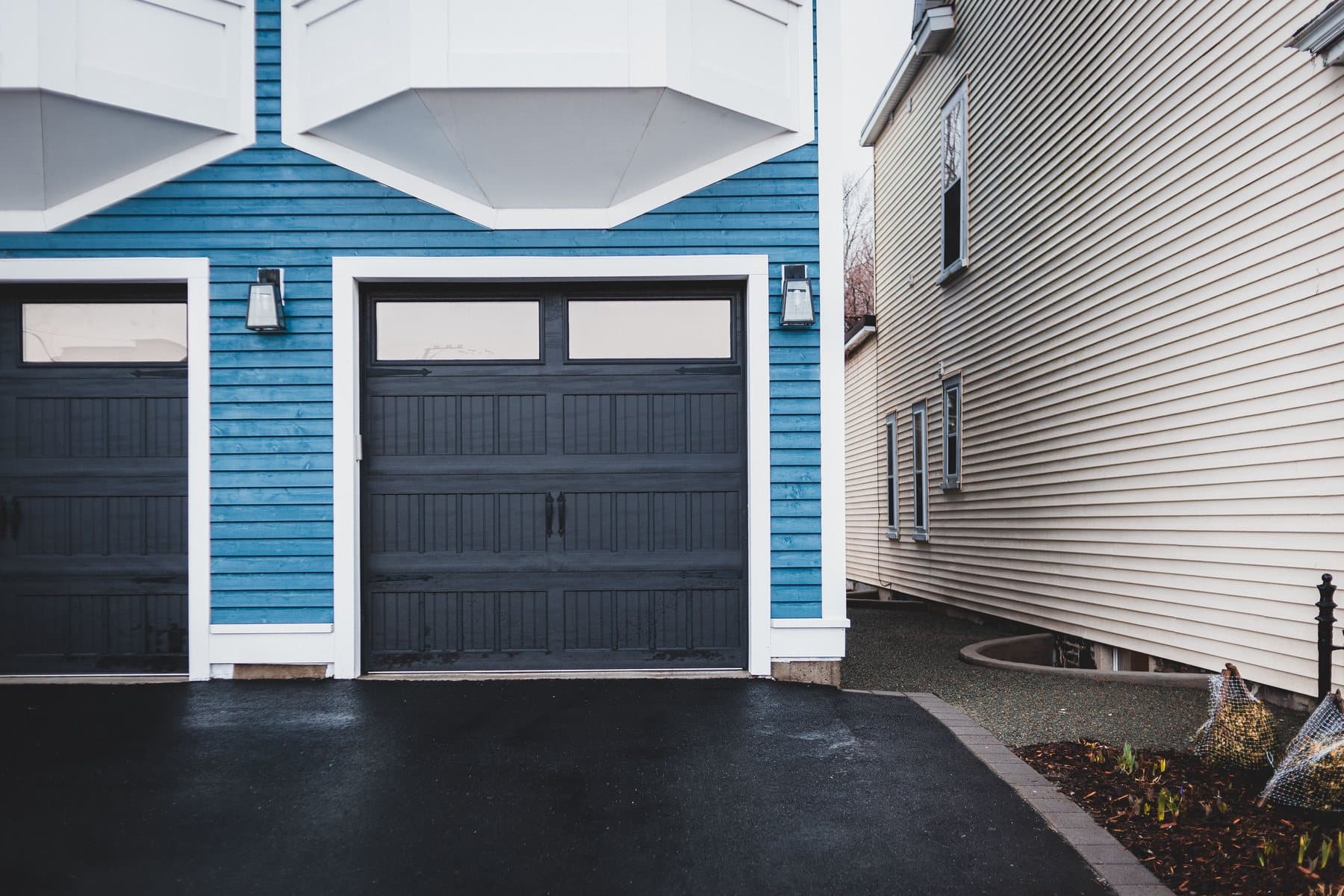 A dark carriage-style steel garage door with a row of window lites, set in blue siding