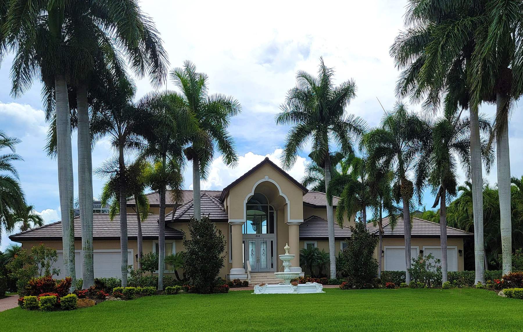 A single-story Florida home behind a wide, freshly cut lawn, framed by tall palms and flower beds
