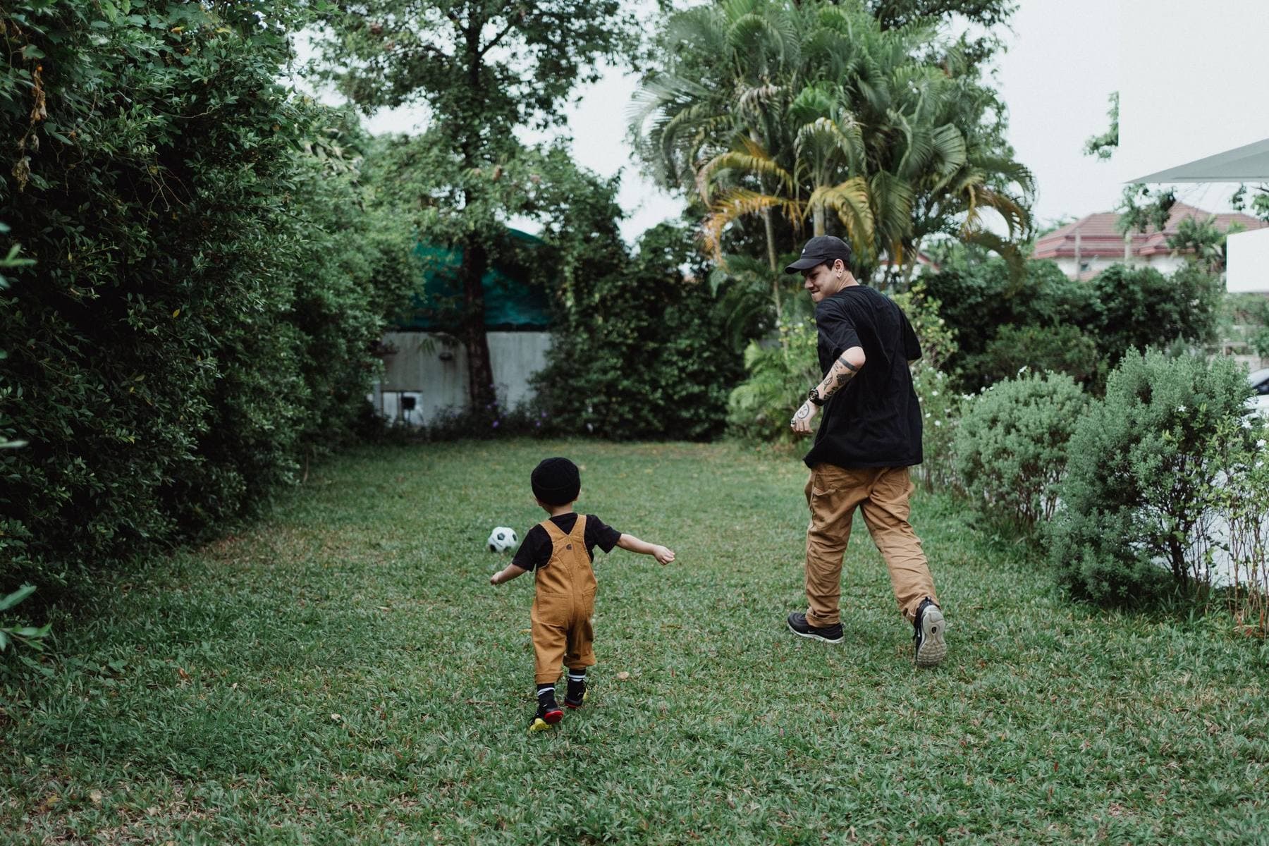A father and a toddler chase a soccer ball across a backyard lawn with palms behind. A photo from Six Oaks Lawn & Landscape, the sample landscaping website.