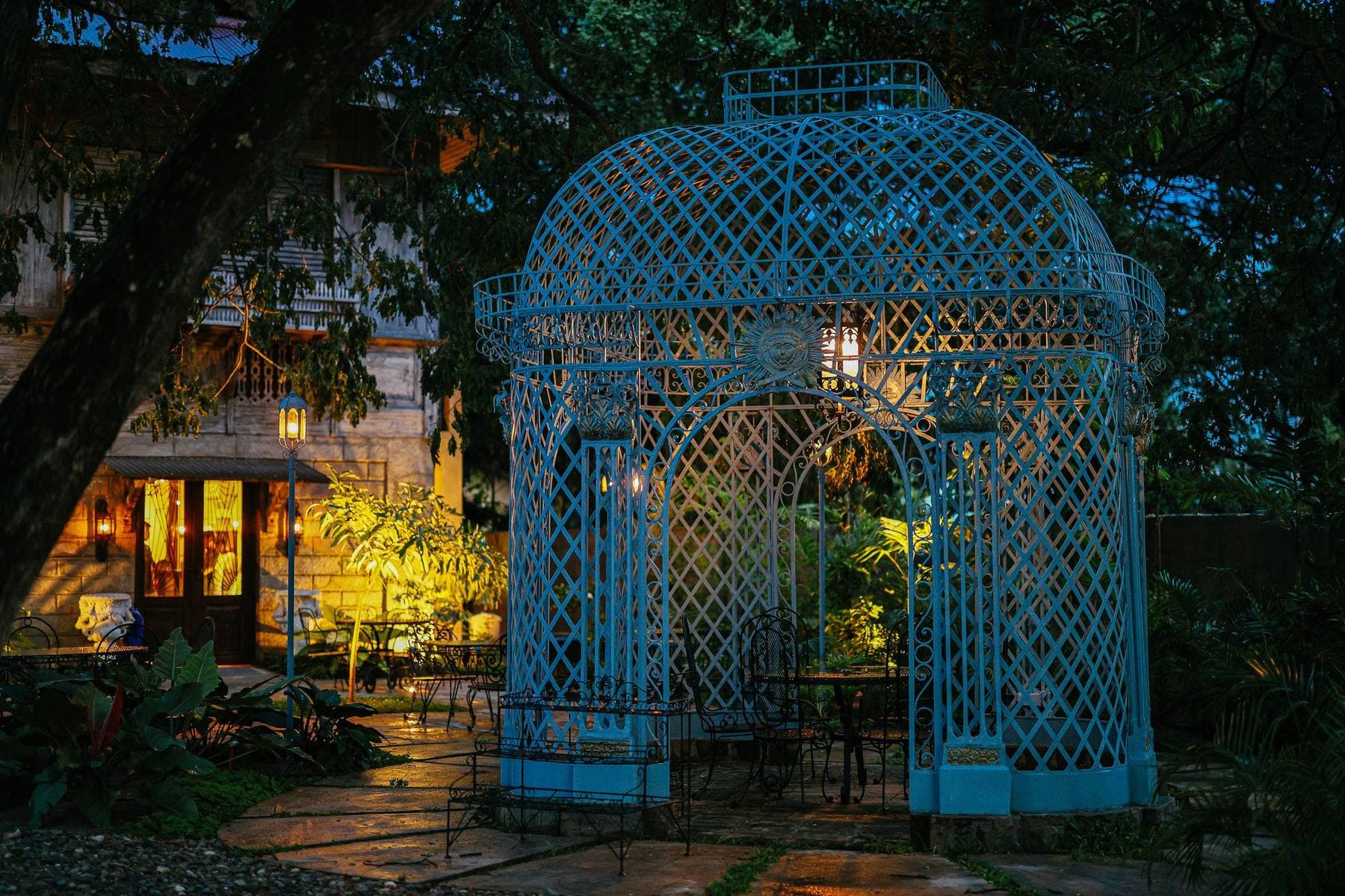 A tropical garden at dusk with warm path lights and a wrought-iron gazebo