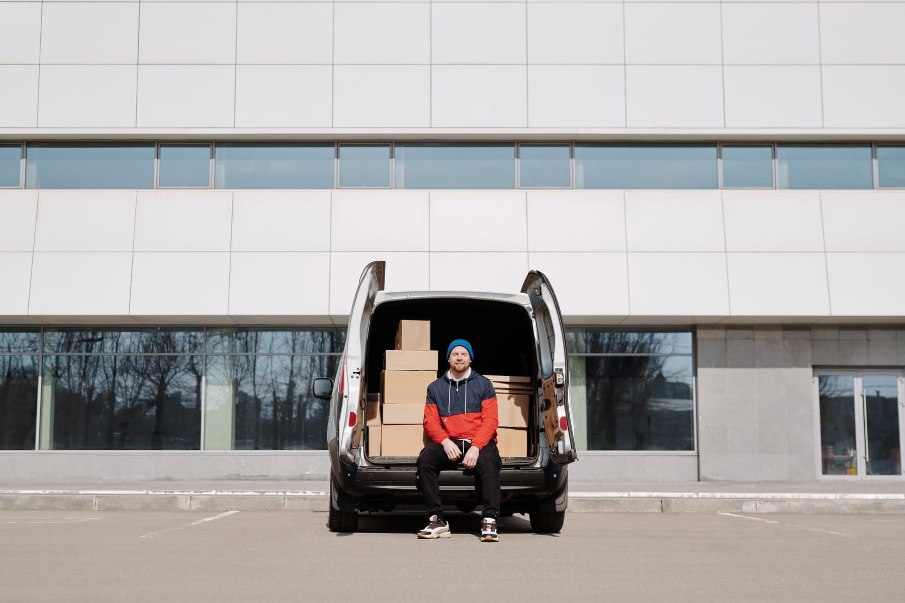 A worker sitting in the open back of a loaded work van outside a business