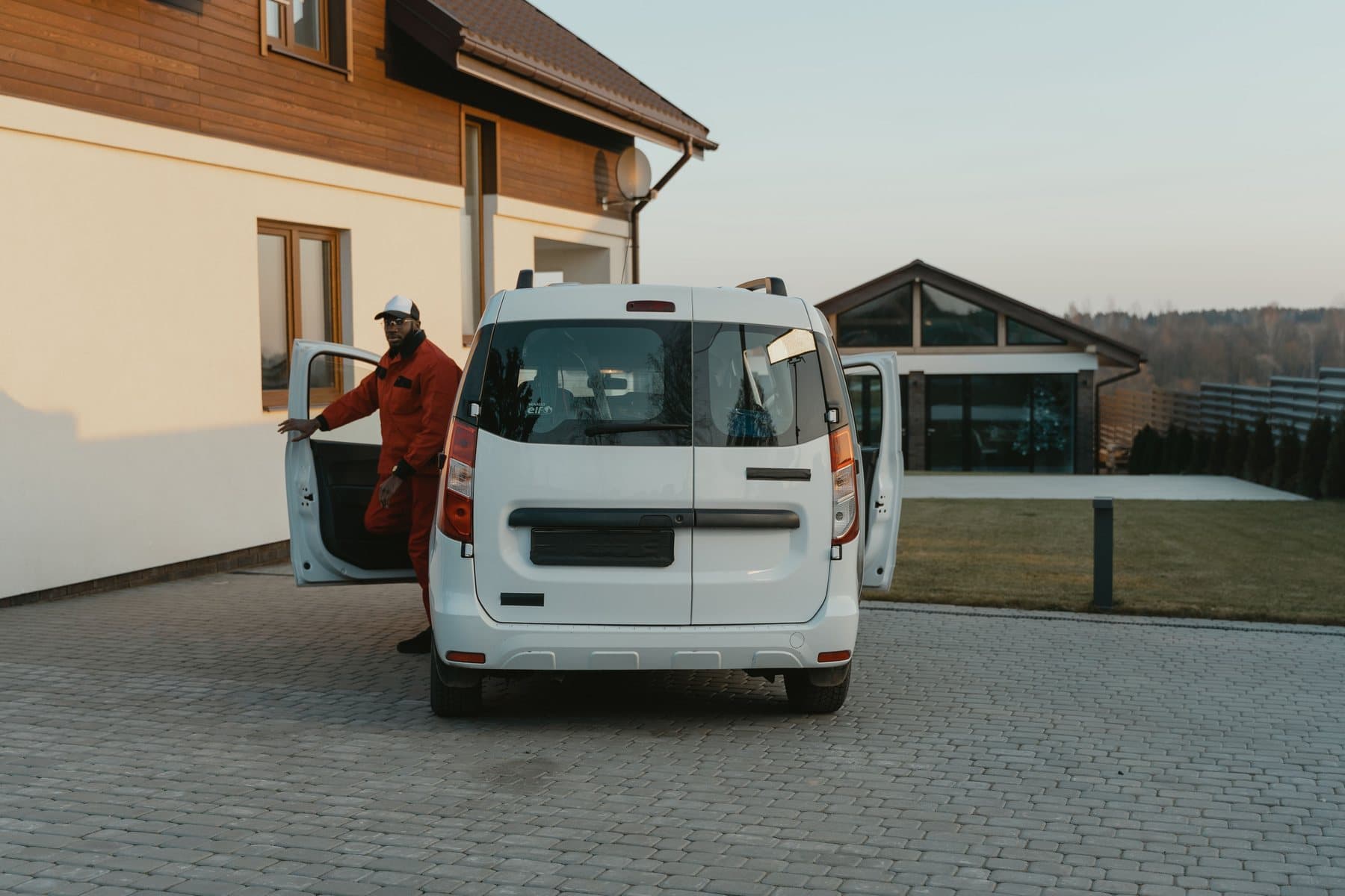 A white work van parked on a paved driveway beside a house in evening light, its side door open
