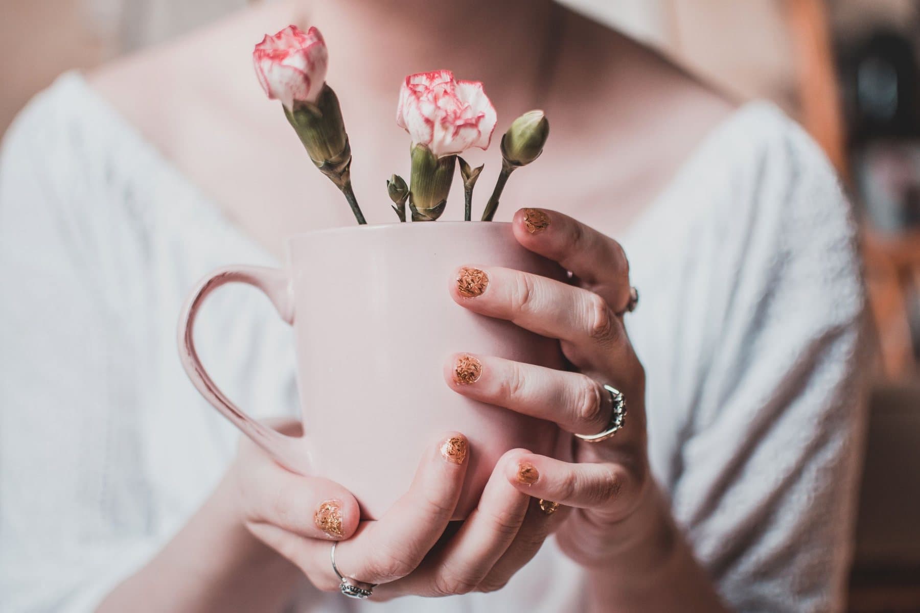 Hands with glittery gold nails holding a pink mug of carnations. A photo from Linden & Lacquer Nail Studio, the sample nail salon website.