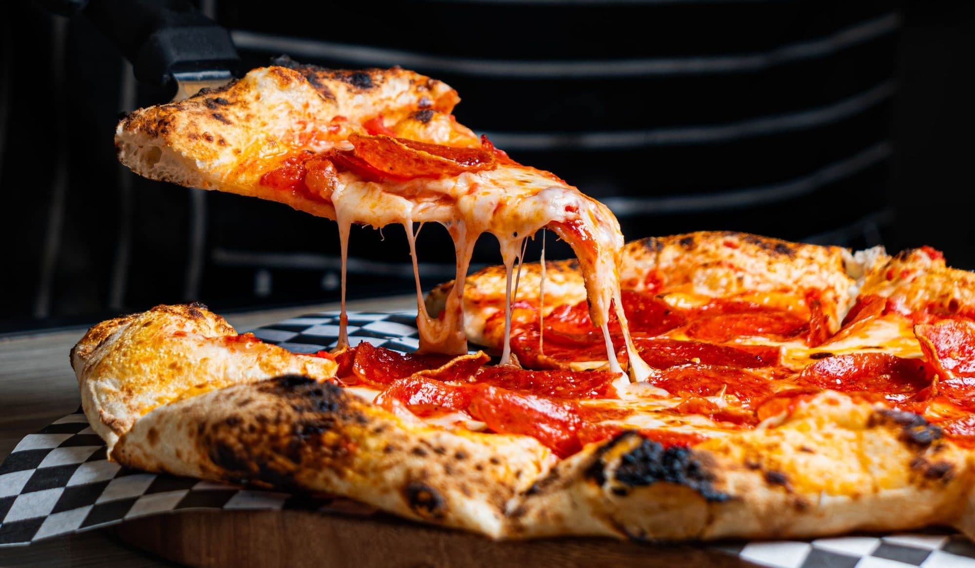 A slice of brick-oven pepperoni pizza lifted with long strings of melted mozzarella