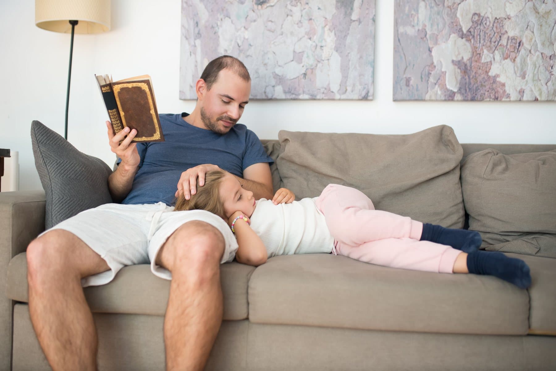 A father reading on the sofa while his daughter sleeps with her head in his lap. A photo from Copperfield Plumbing & Air, the sample plumbing & HVAC website.