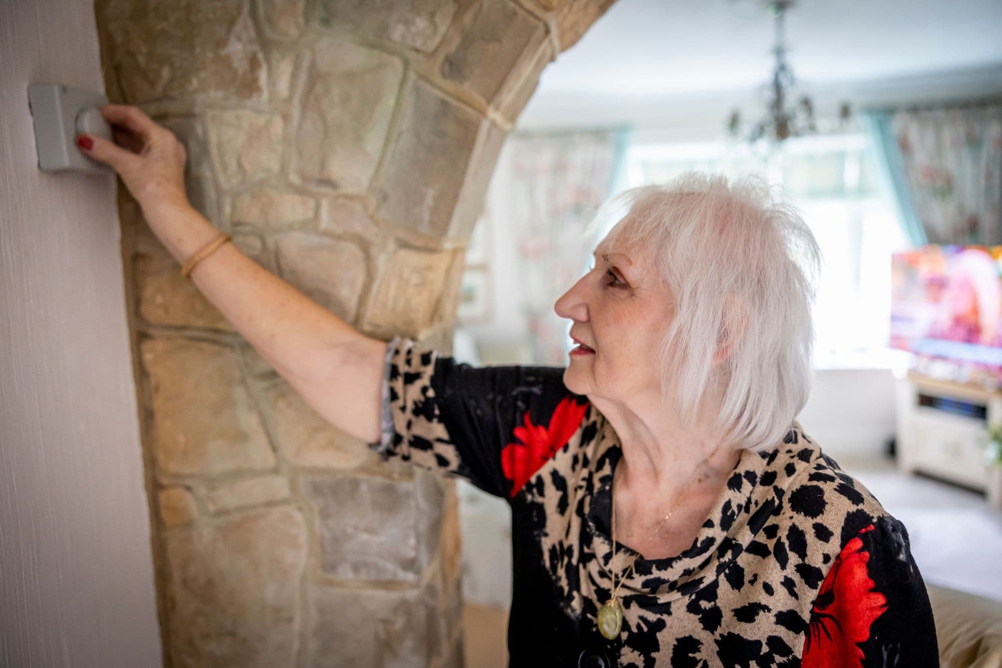 A woman reaching up to adjust the thermostat on a stone-clad wall in her living room