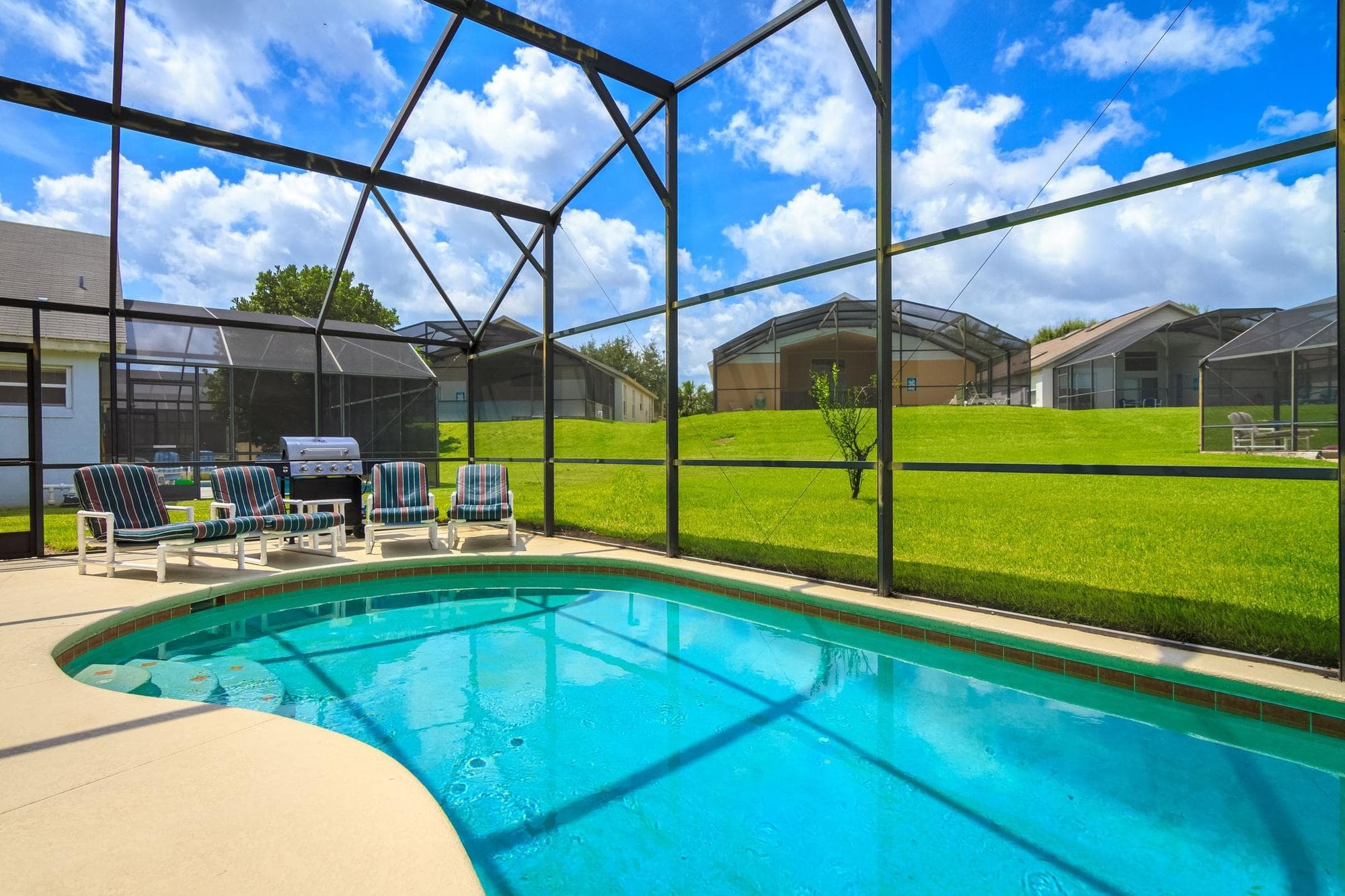 A screened pool behind a Winter Park home with clear turquoise water, patio chairs and a grill