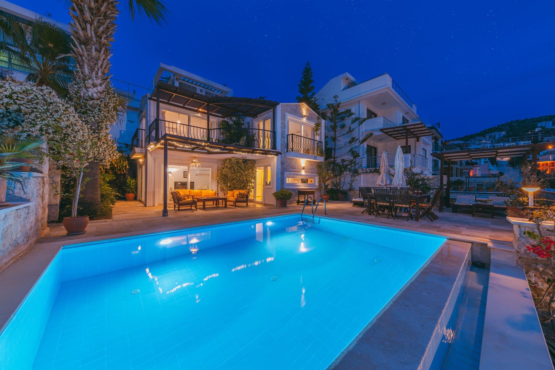A pool lit from underwater at night beside a lit house and terrace