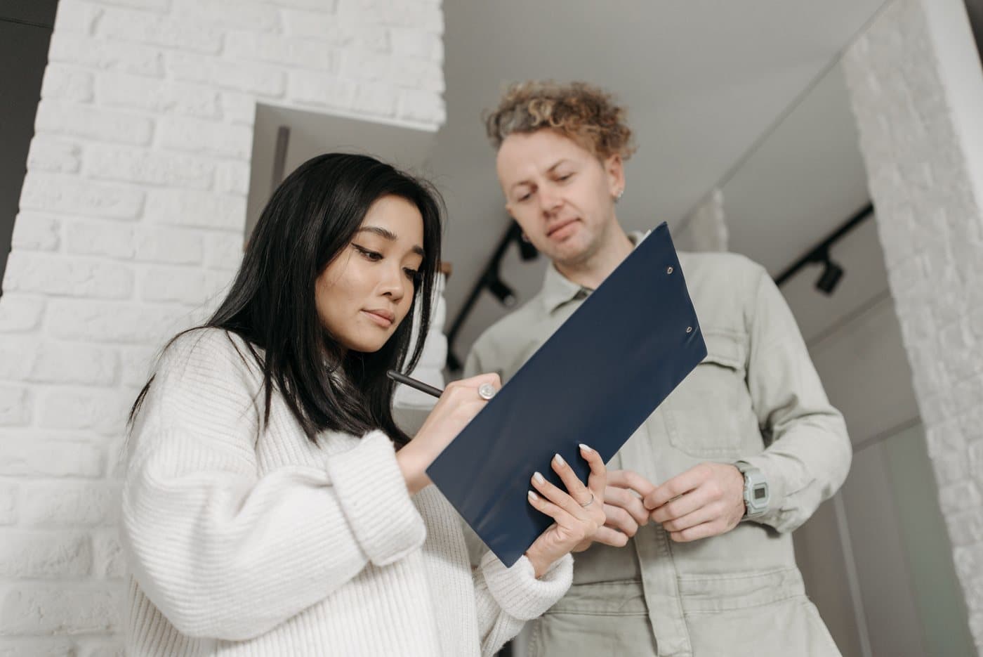 A woman writing on a clipboard held by a man in work overalls