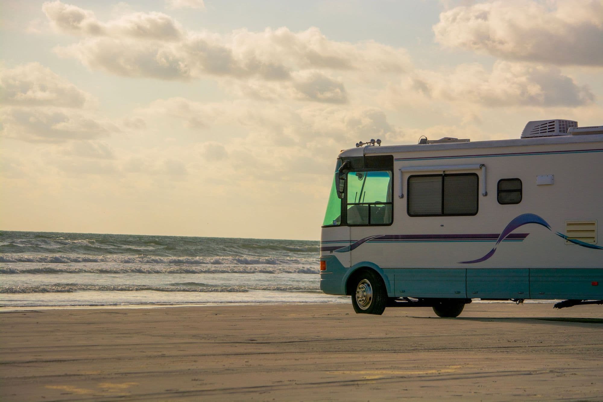 A motorhome parked on firm sand beside the Gulf at sunset, waves rolling in