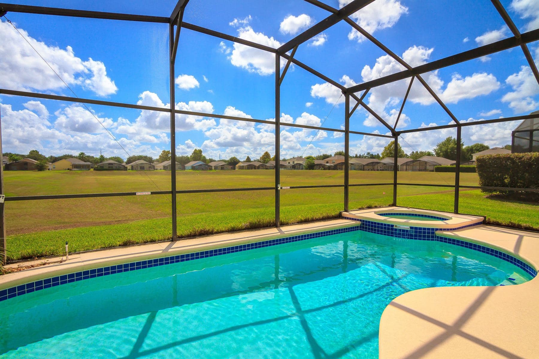 A screen pool enclosure over a pool and spa, open lawn beyond the mesh