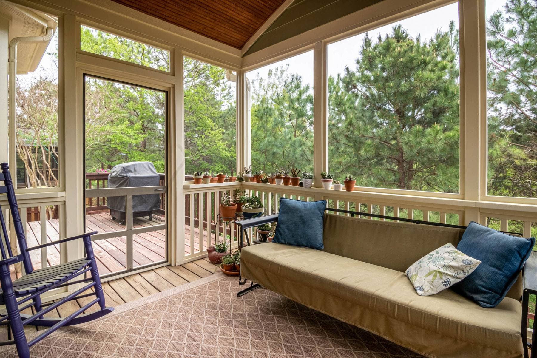 A screened porch with a sofa, a rocker and potted plants, screen door out to the deck