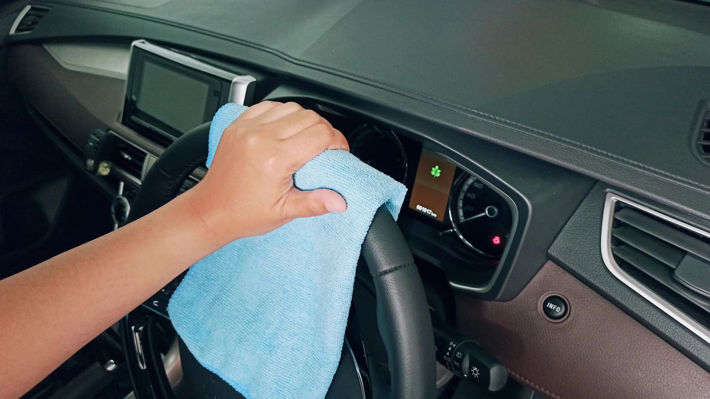 A hand wipes a car dashboard and steering wheel with a blue microfibre cloth.
