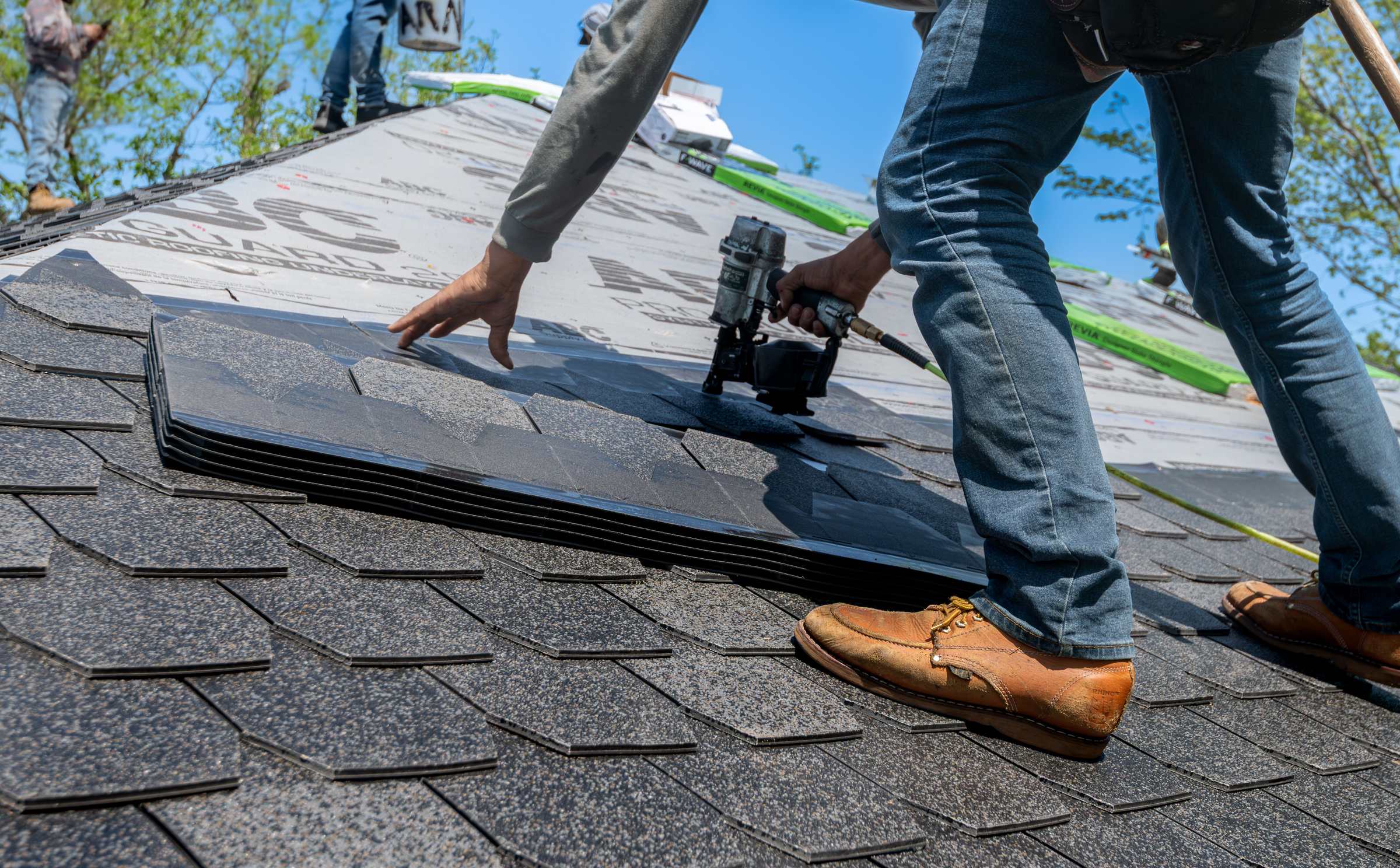 A roofer fixing shingles with a nail gun, boots on the finished course