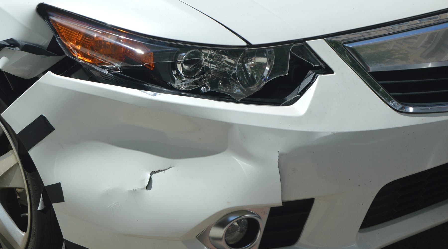 A white sedan with a pushed-in front bumper and a broken headlamp