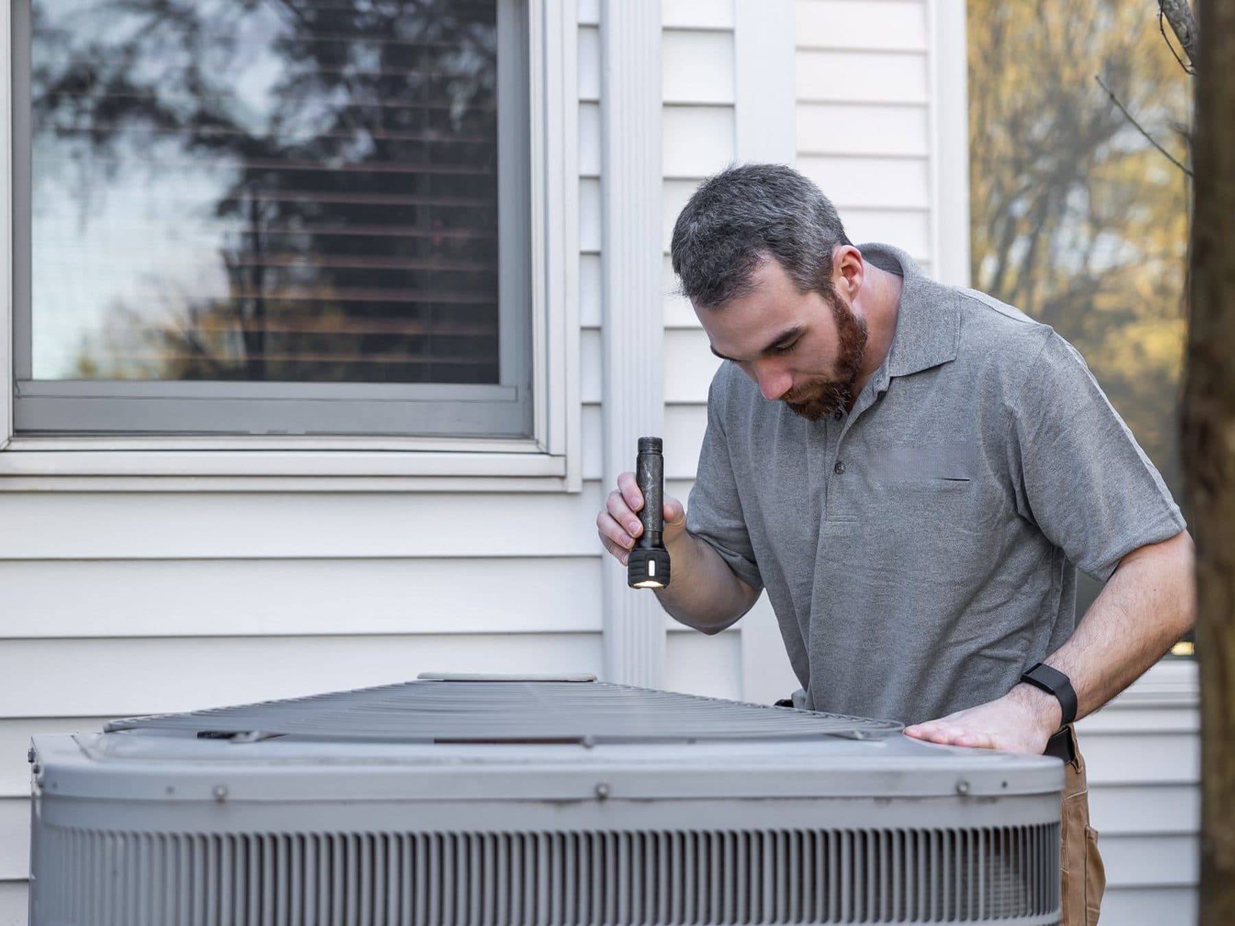 A heating and cooling technician at work A heating and cooling technician checking an outdoor AC unit with a flashlight