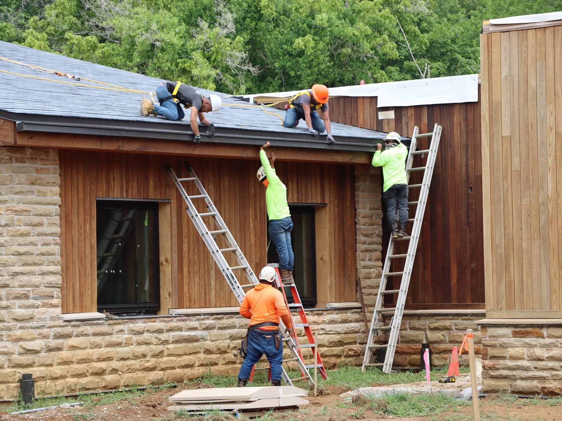 A roofing crew at work A roofing crew installing gutters along the eaves of a stone house, on ladders