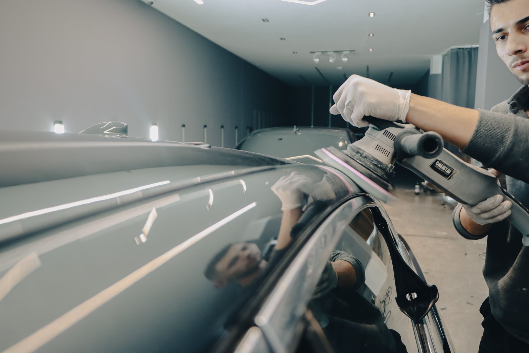 Hand-polishing the paintwork of a dark car with a machine polisher