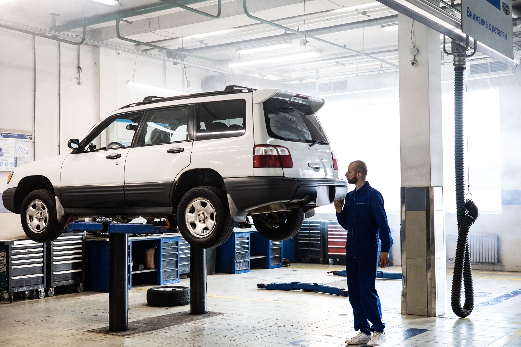 A technician beside an SUV raised on a two-post lift in a daylit repair bay