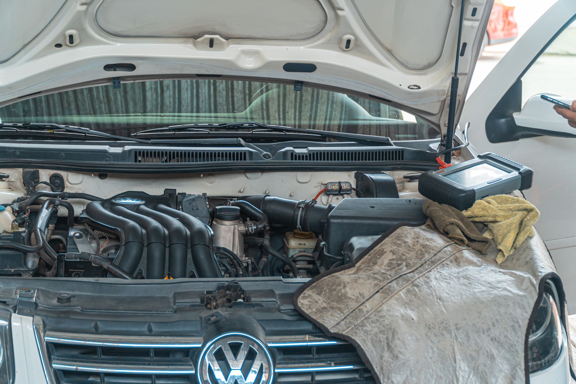 Two technicians reading live data from a scan tool and laptop over an open engine bay