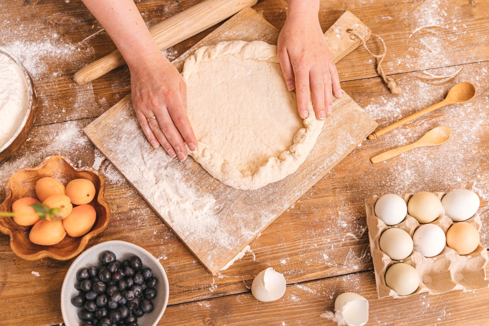 Floured hands pressing the edge of a round of dough on a wooden board