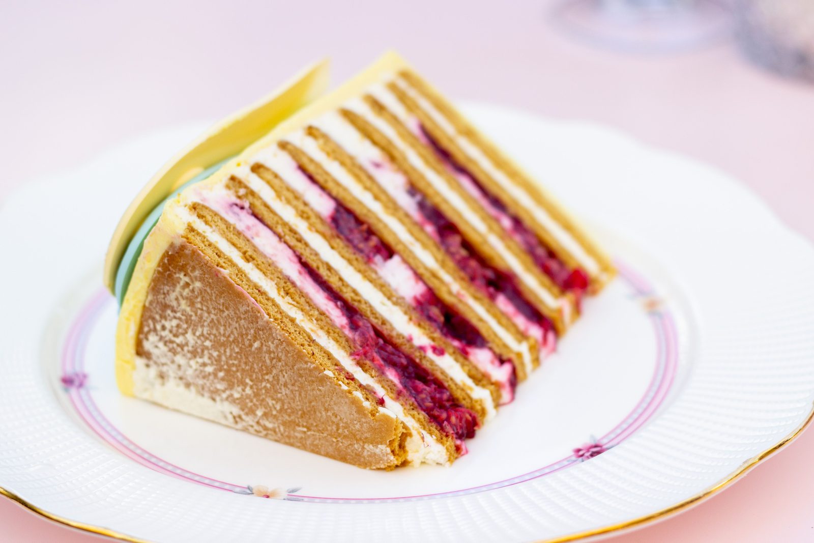 A slice of many-layered cake with raspberry and cream filling on a white plate