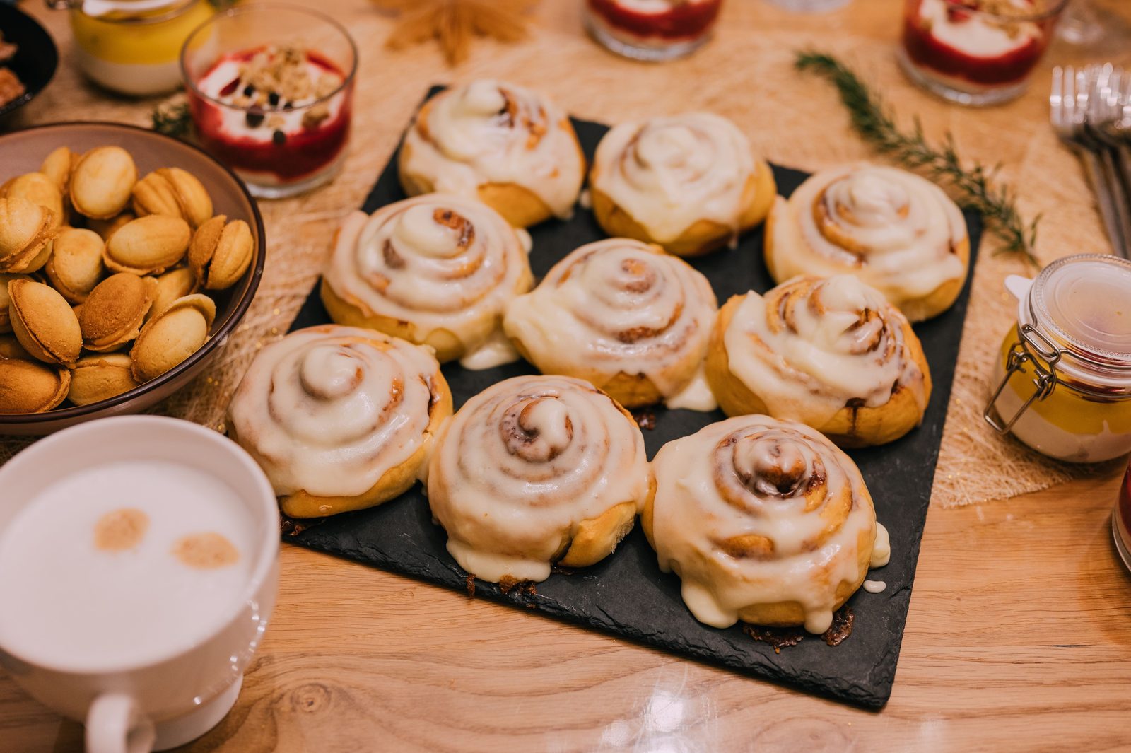 Nine cinnamon rolls with cream cheese icing on a black slate board