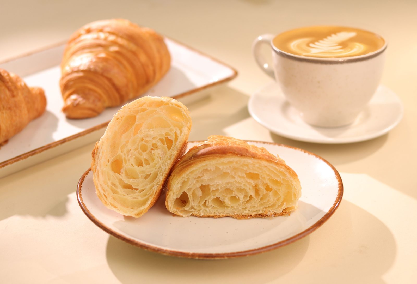 A sliced croissant with an airy crumb beside a latte with foam art