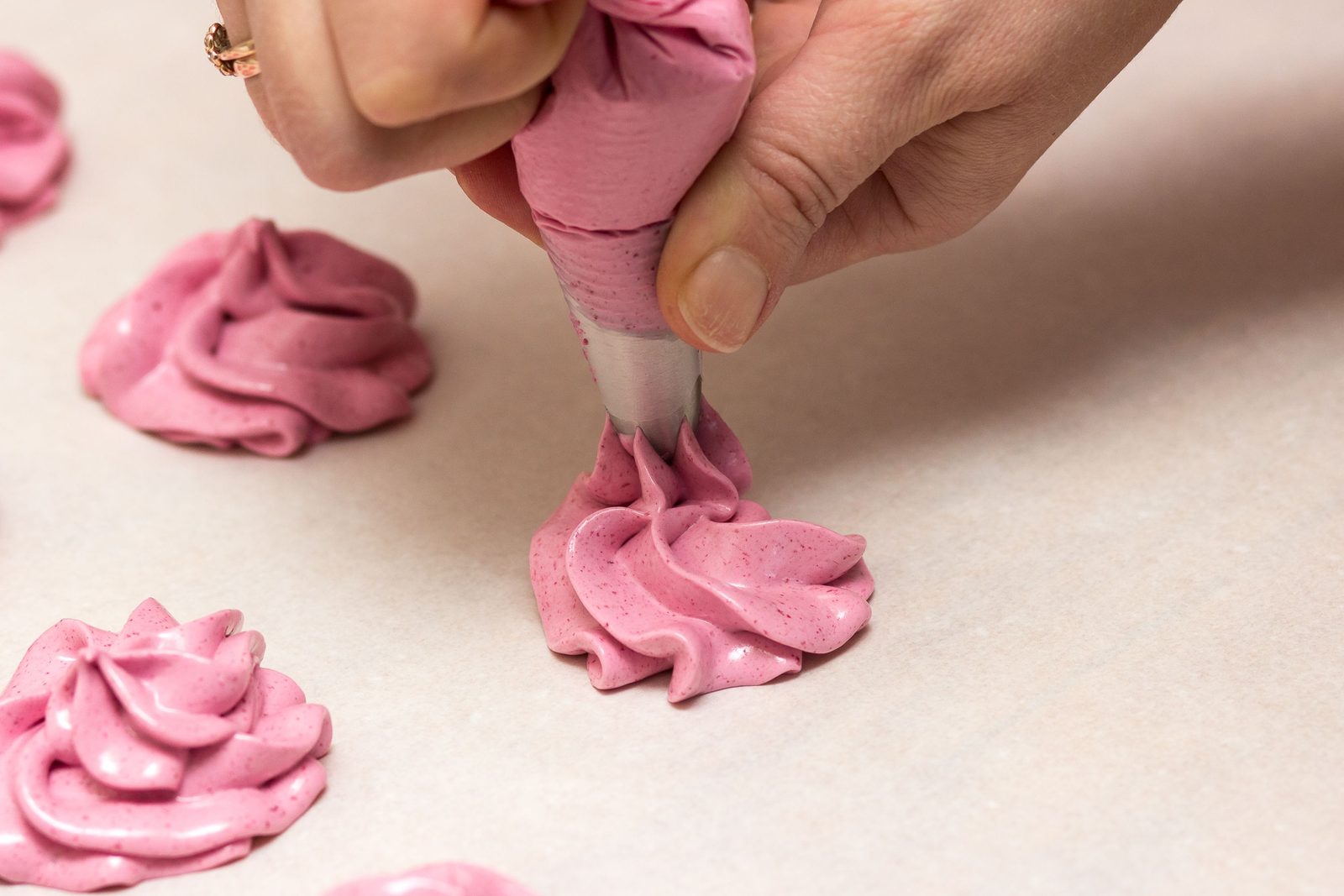 A hand squeezing a pink piping bag to form a frosting rosette