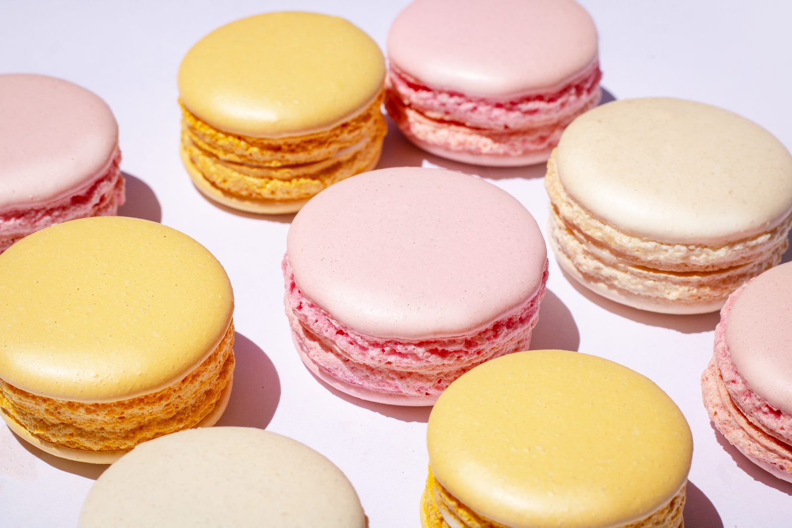 Pink, butter-yellow and cream macarons arranged close together on a pale table