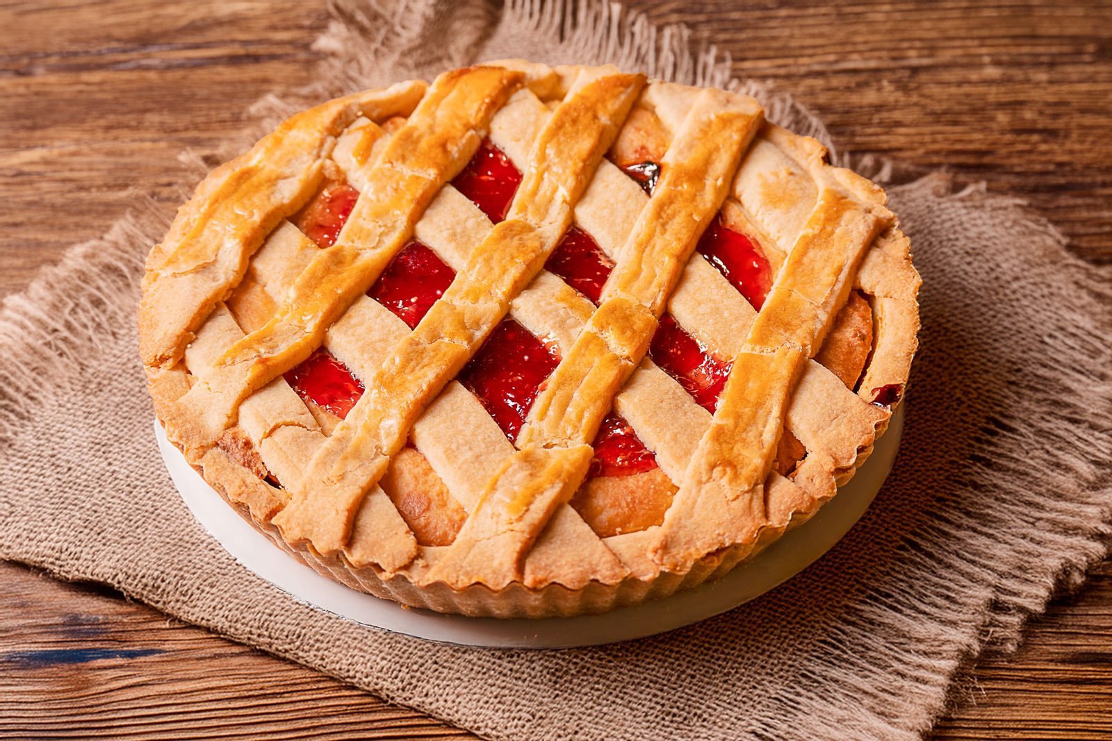 A whole lattice-top pie with bright red filling showing through the golden crust