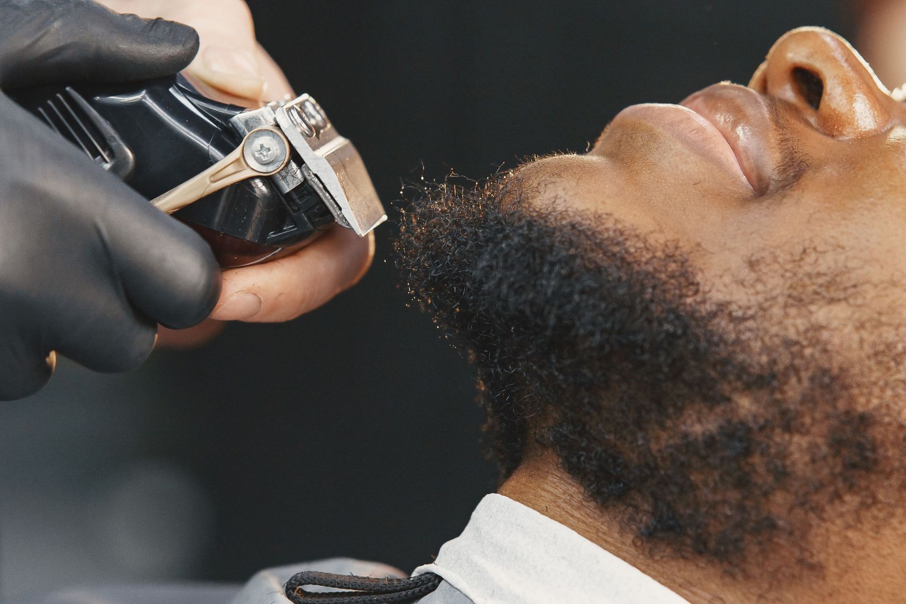 A beard being trimmed with clippers, the client’s chin tipped up