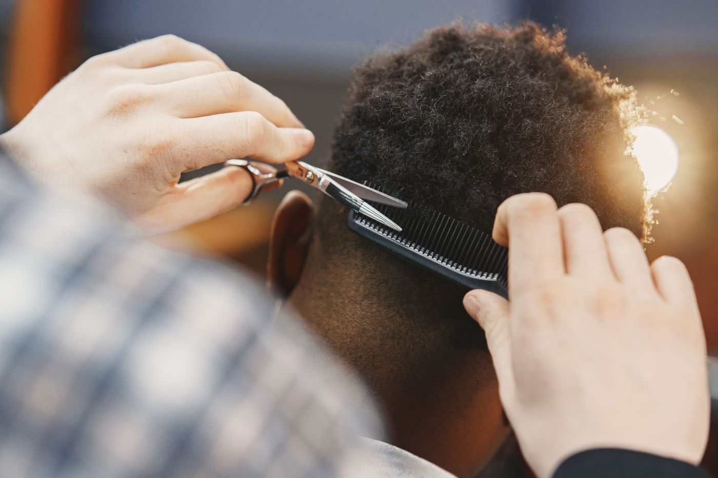 Shaping coily hair with shears over a comb, warm light behind