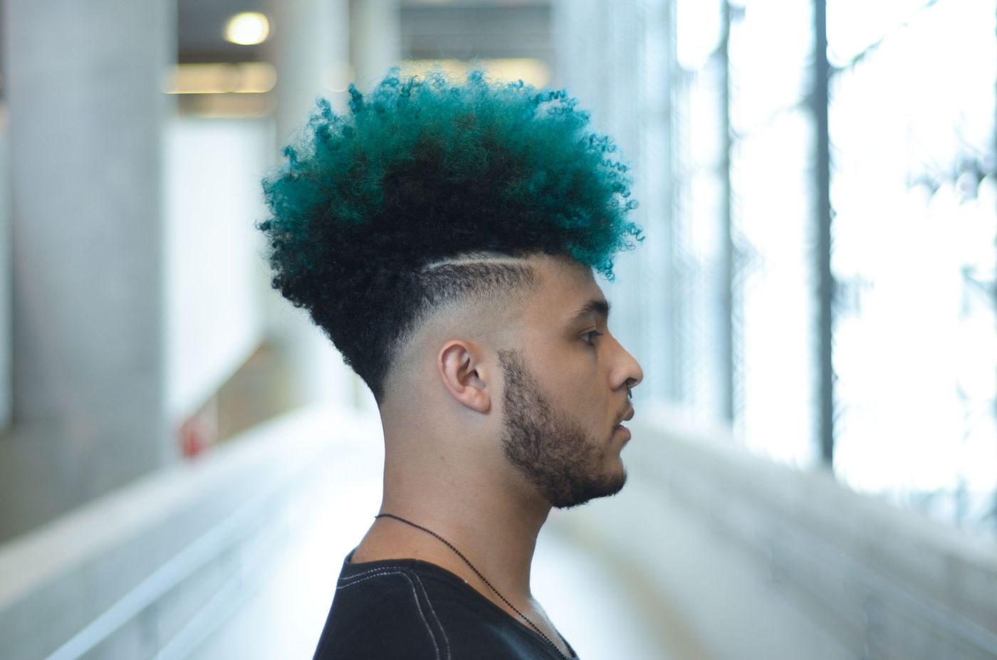 A curly top dyed teal with a low taper and a razor part, side profile