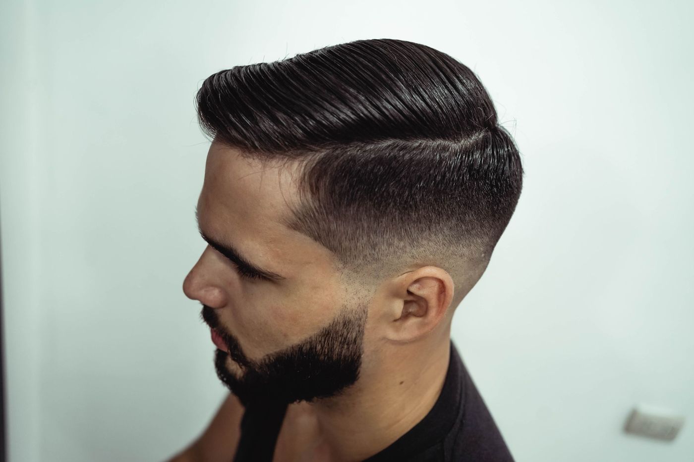 A side part with a taper and a groomed beard, side profile
