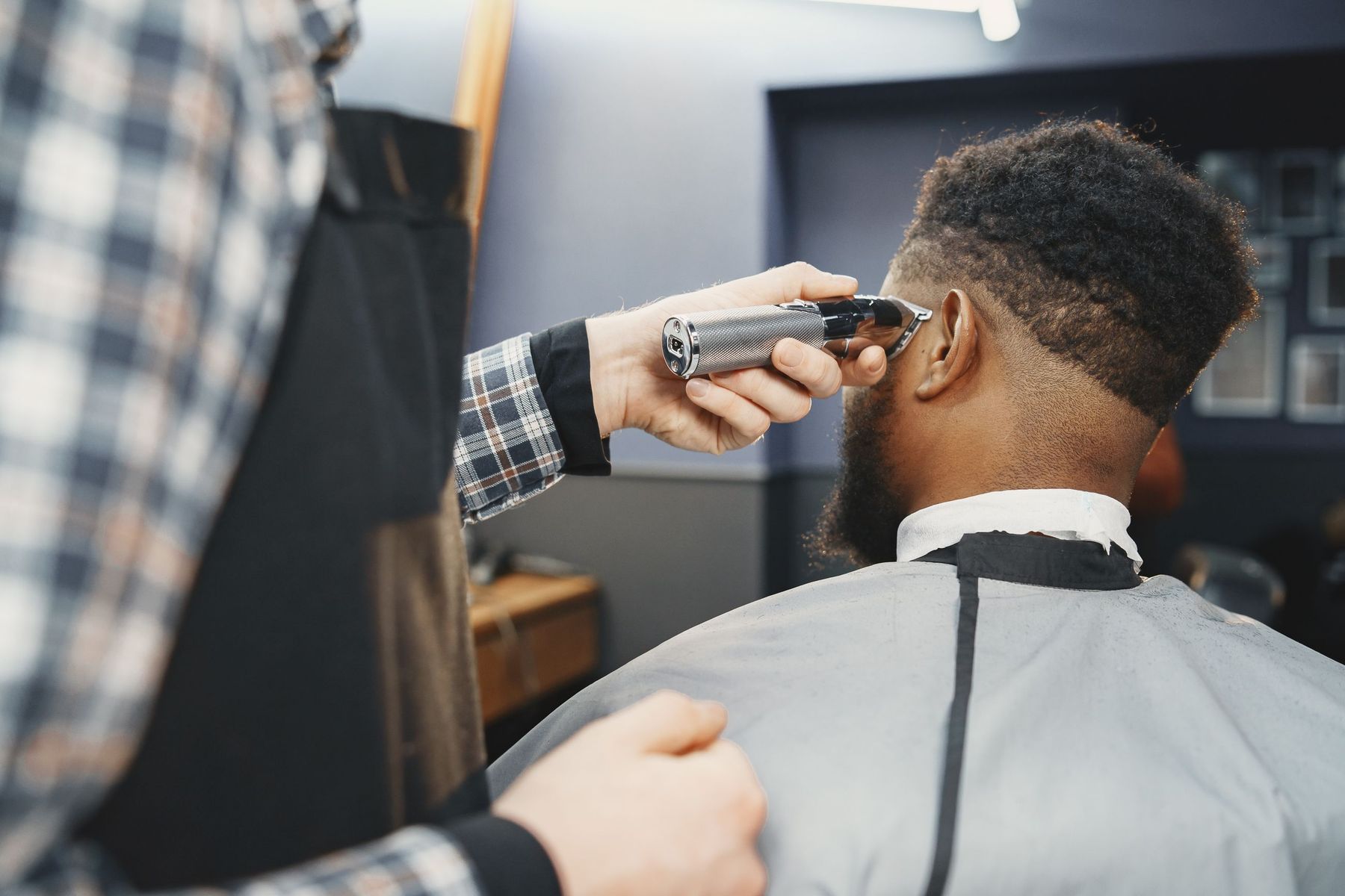 A barber running a trimmer up the side of a client’s head from behind