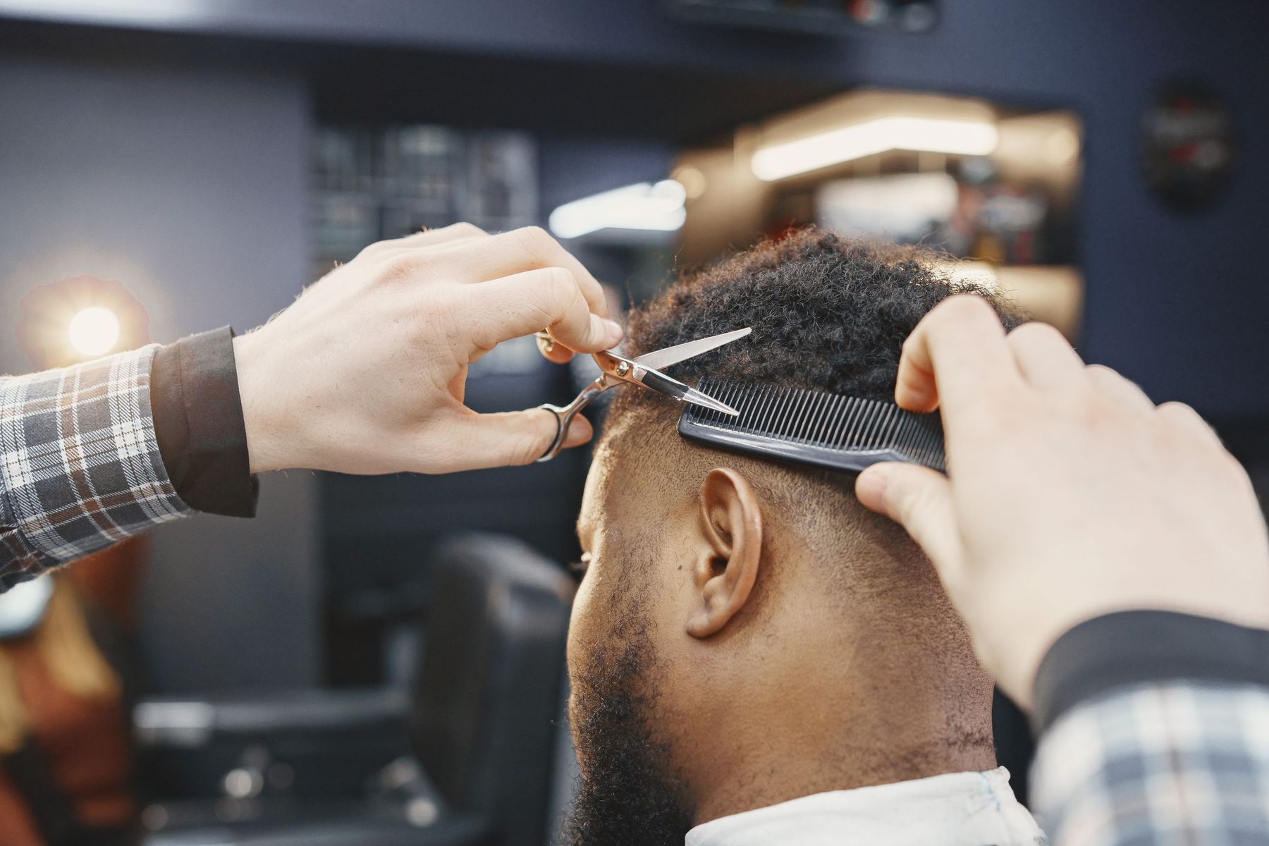 A barber lifting hair over a comb and cutting it with scissors at the back of a client’s head