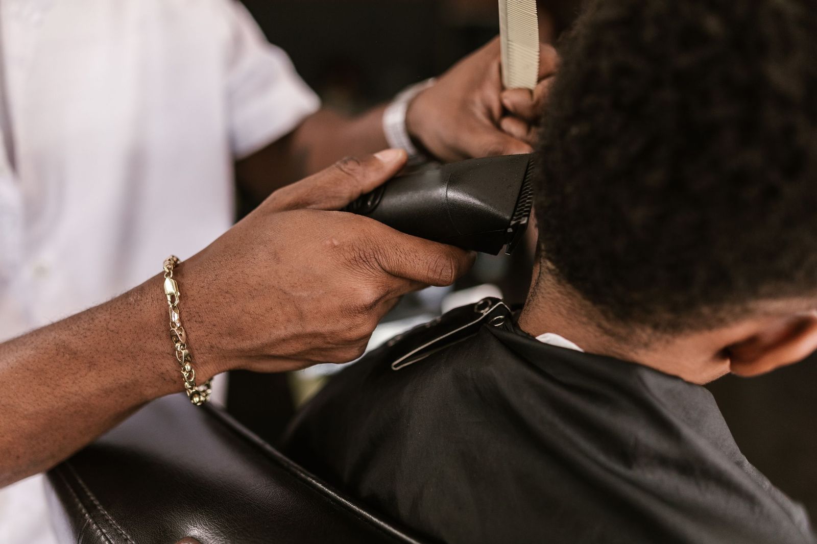 Clippers and a comb working up the back of a boy’s head, seen from behind in the chair