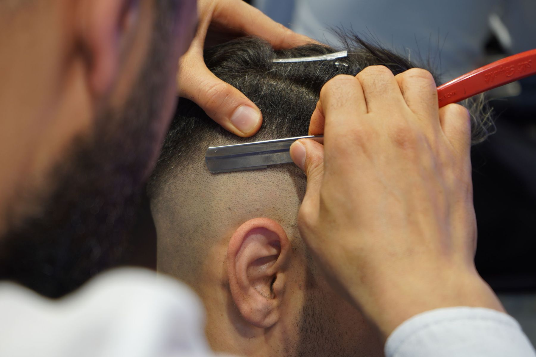 A barber cutting a sharp part line with a straight razor above the ear